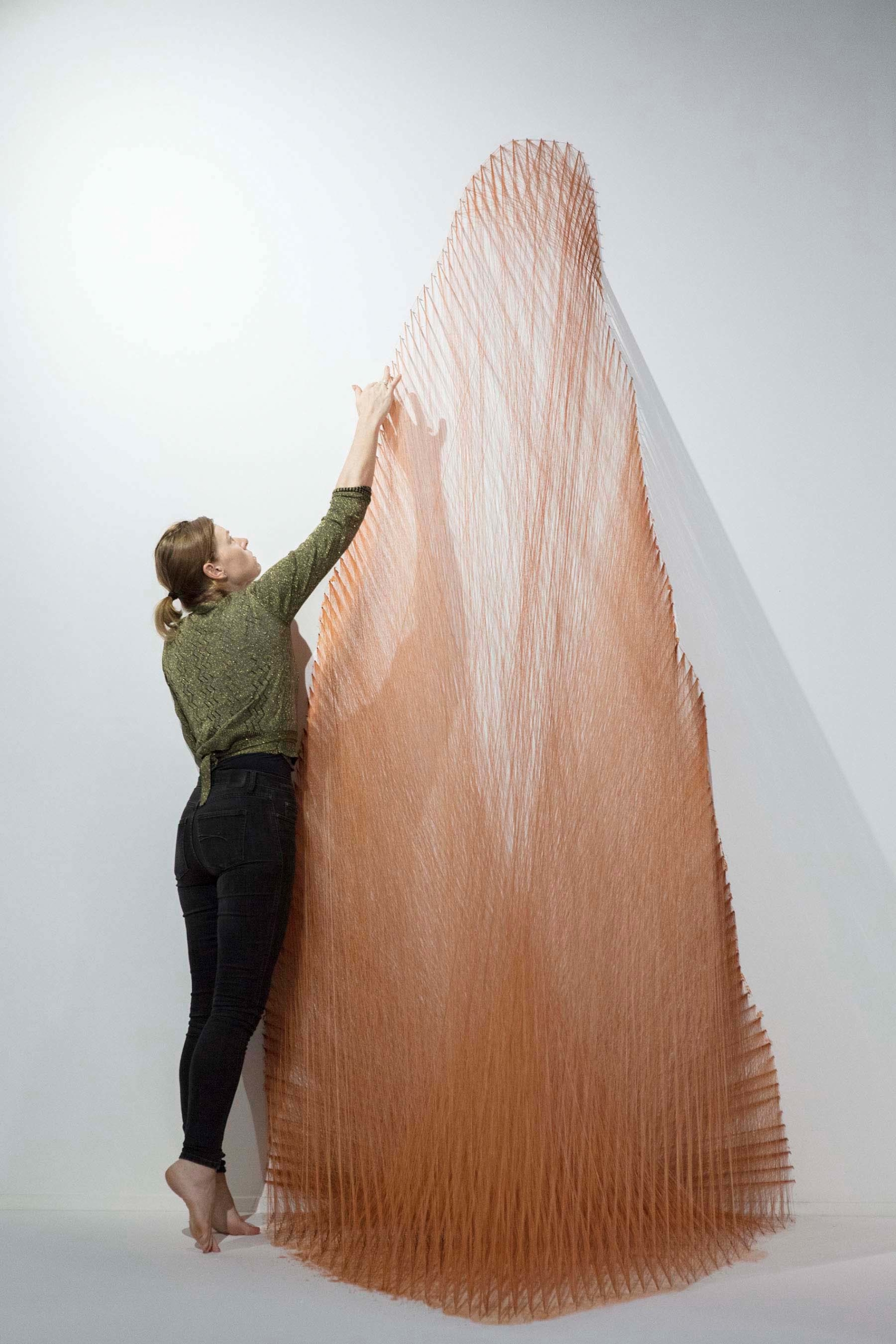 woman reaching up to the top of a large artwork made of ochre dyed string